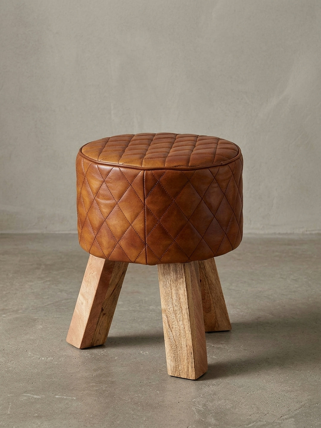 Moderner Sitzhocker mit rundem Polster aus braunem Echtleder und drei Beinen aus massivem Mango-Holz, freigestellt auf weißem Hintergrund, Frontansicht._