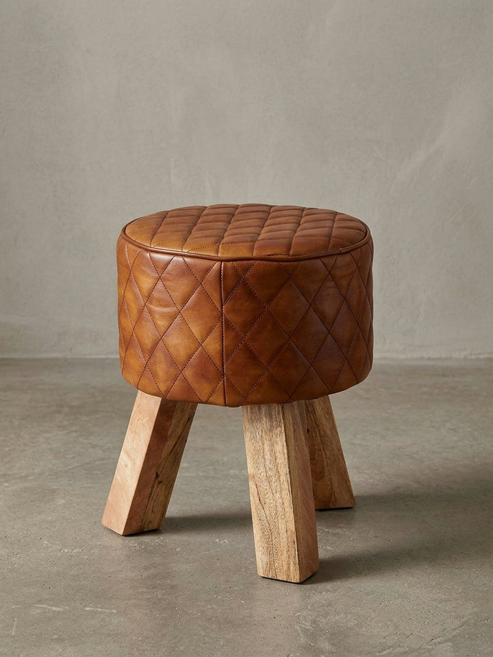 Moderner Sitzhocker mit rundem Polster aus braunem Echtleder und drei Beinen aus massivem Mango-Holz, freigestellt auf weißem Hintergrund, Frontansicht._