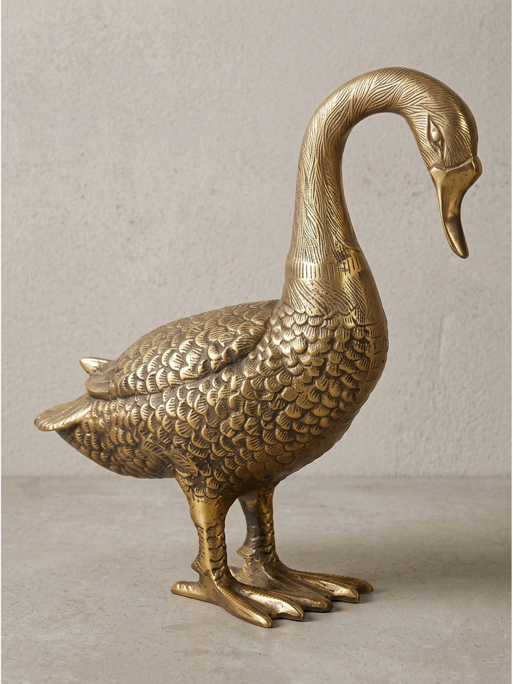 Frontale Seitenansicht der goldenen Tierfigur Gans aus massivem Aluminium, die geschwungene Halslinie und das detailreiche Federkleid wirken besonders elegant freigestellt vor einem neutralen Hintergrund._