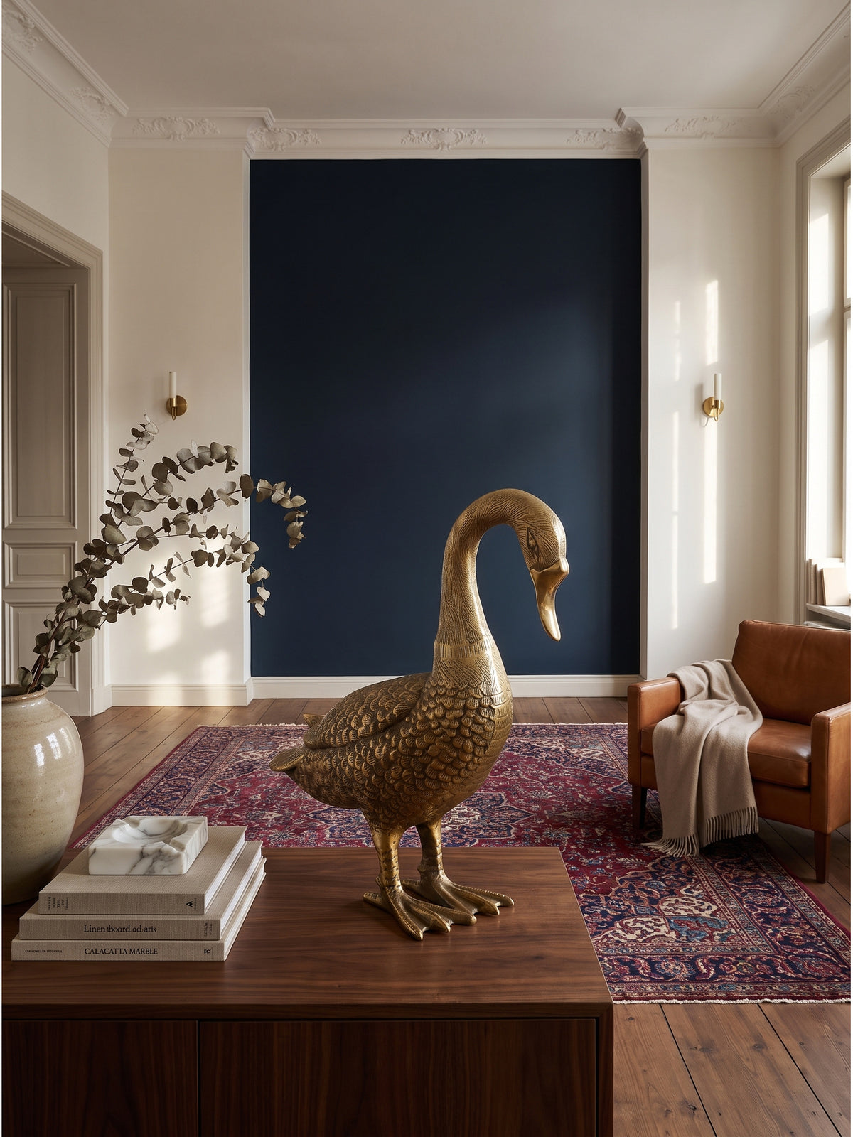 Große Dekofigur Gans aus golden lackiertem Aluminium 46x19x42 cm als elegantes Statement-Piece auf einem dunklen Walnuss-Sideboard in einem klassisch modernen Wohnzimmer vor nachtblauer Wand._