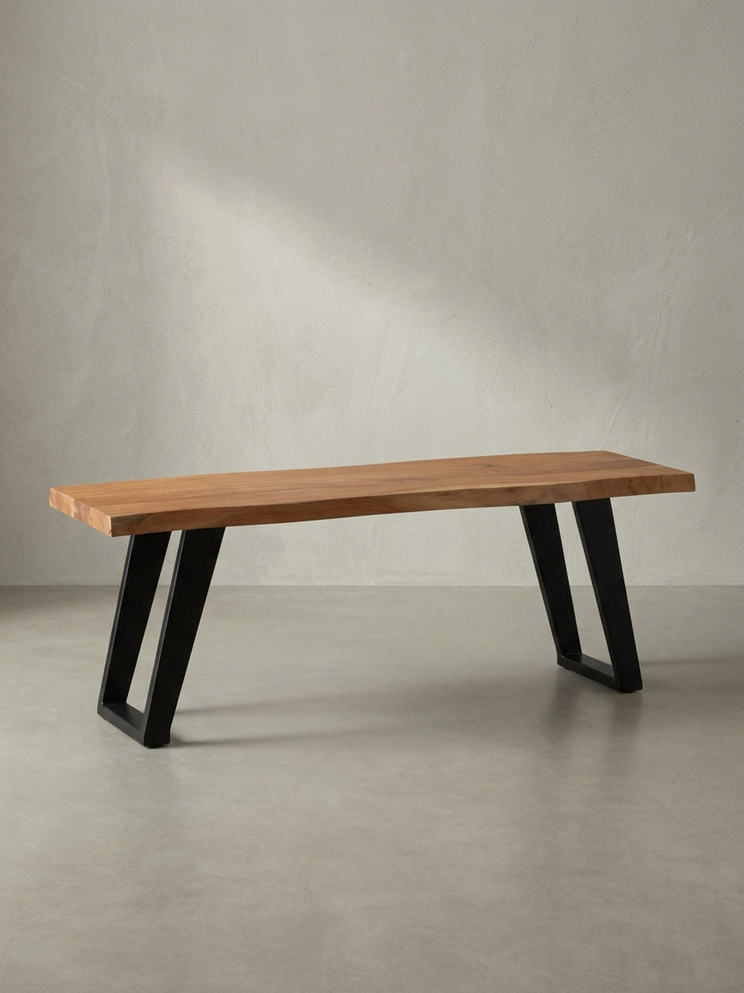 Freigestellte Garderobenbank aus Akazie Massivholz mit schwarzem Metallgestell, die natürliche Baumkante der Sitzfläche ist das zentrale Designmerkmal._