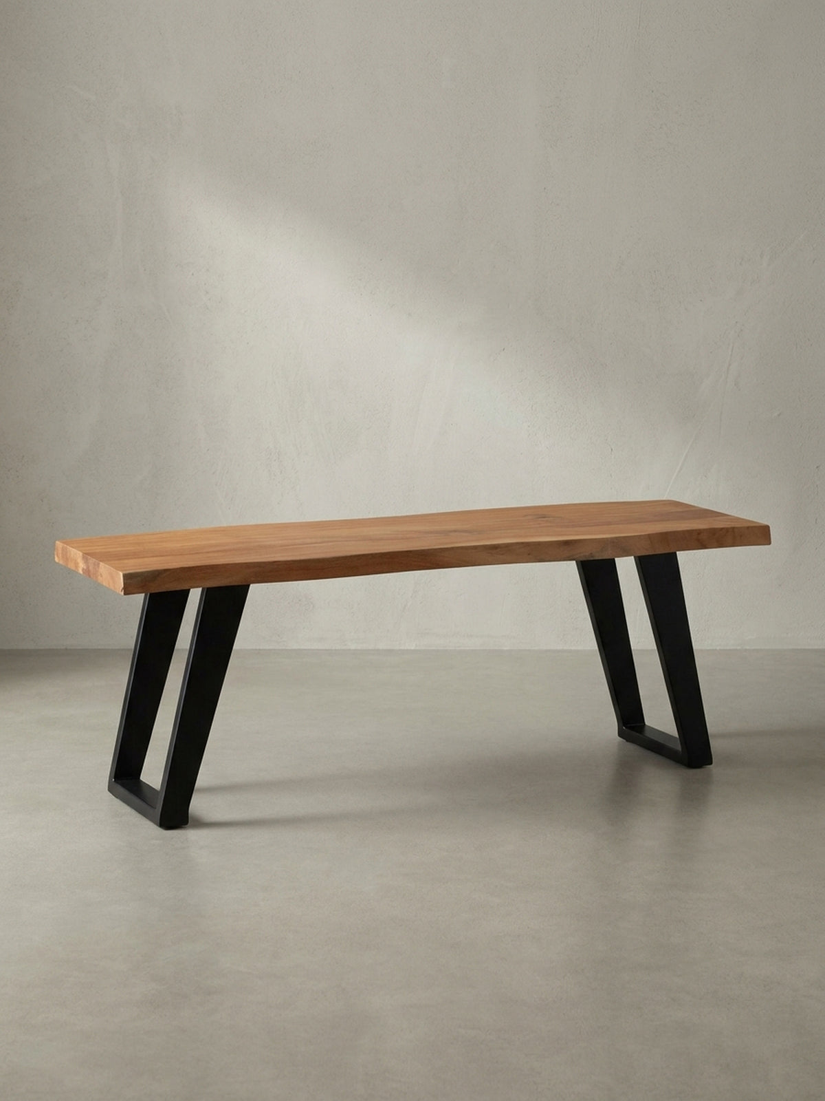 Freigestellte Garderobenbank aus Akazie Massivholz mit schwarzem Metallgestell, die natürliche Baumkante der Sitzfläche ist das zentrale Designmerkmal.