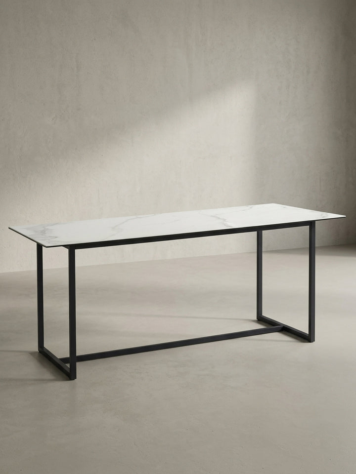 Freigestellter rechteckiger Esstisch 180x90x76 cm mit robuster Keramikplatte in Marmoroptik und mattschwarzen Metallbeinen von vorne links_
