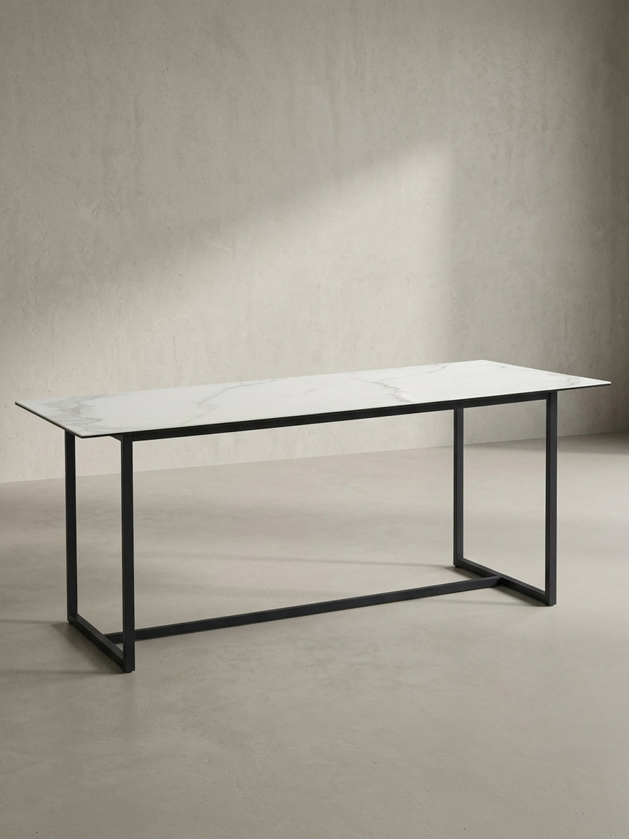 Freigestellter rechteckiger Esstisch 180x90x76 cm mit robuster Keramikplatte in Marmoroptik und mattschwarzen Metallbeinen von vorne links_