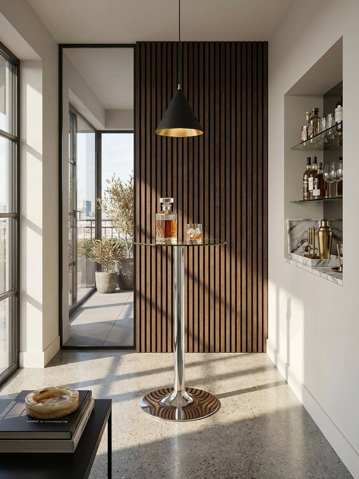 Ein runder Stehtisch aus transparentem Glas und Chrom steht als glänzender Mittelpunkt in einer exklusiven Heimbar mit dunkler Holzlamellenwand und fugenlosem Betonboden._