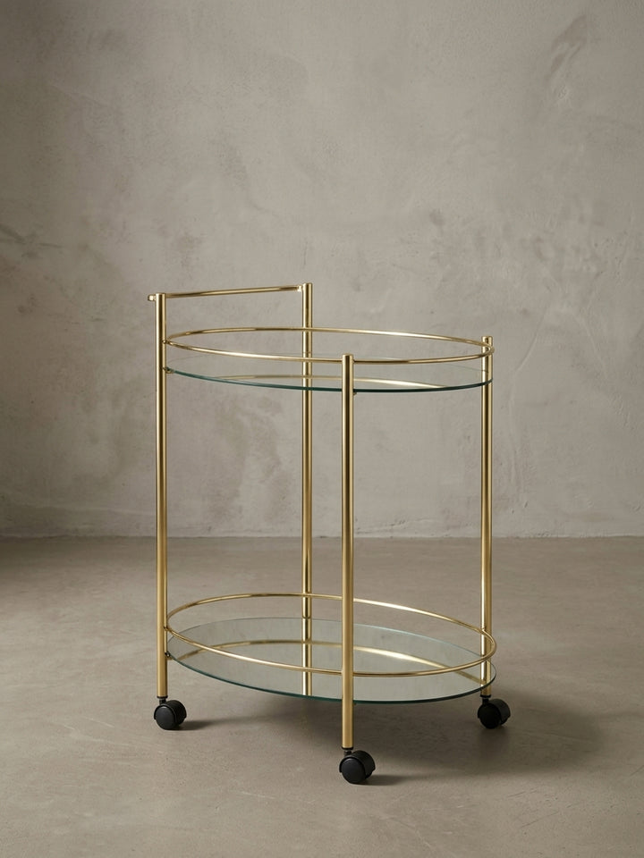 Seitenansicht des Teewagens auf Rollen, die seine schlanken Proportionen mit 79 cm Höhe und das filigrane goldene Gestell aus Stahl zeigt._