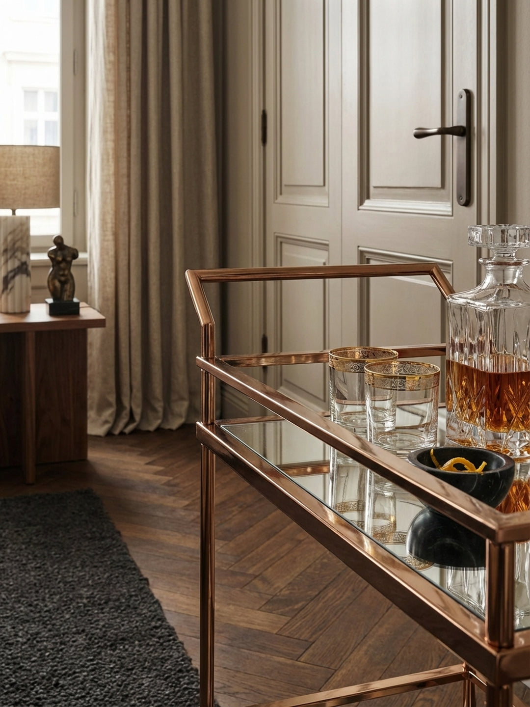 Nahaufnahme der glänzenden, roségold lackierten Stahlstruktur und der spiegelnden Glasablage des Teewagens, die das luxuriöse Finish des Materials zeigt._