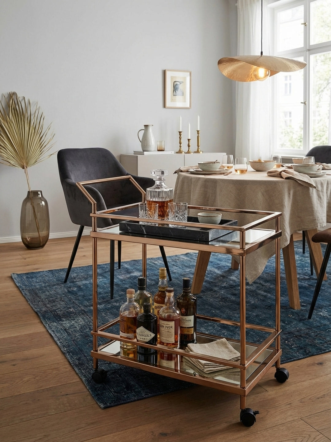 Der elegante Servierwagen in Roségold mit verspiegelten Glasböden steht stilvoll in einem luxuriösen Wohnzimmer mit Holzboden und dient als mobile Cocktailbar._