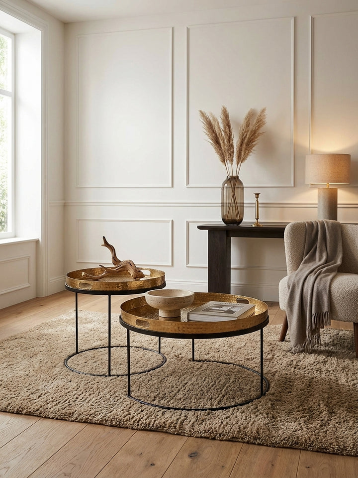 Eleganter Couchtisch im 2er Set in einem modernen Wohnzimmer, die goldenen Hammerschlag-Tabletts auf dem schwarzen Metallgestell harmonieren mit einem dunklen Sofa._
