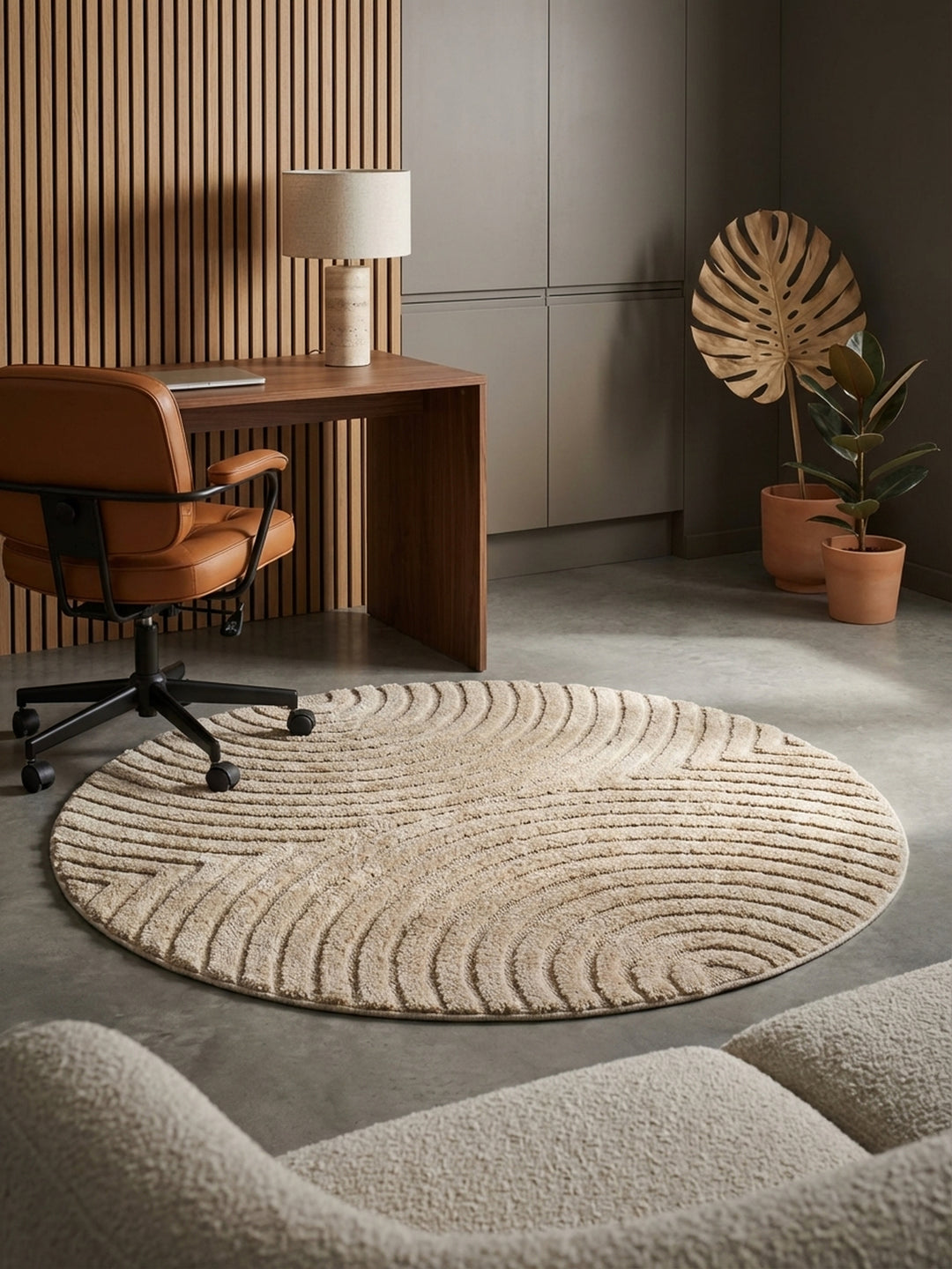 Moderner beigefarbener Teppich mit 3D-Struktur auf poliertem Betonboden in einem Home Office mit Schreibtisch aus Walnussholz und Lederstuhl._