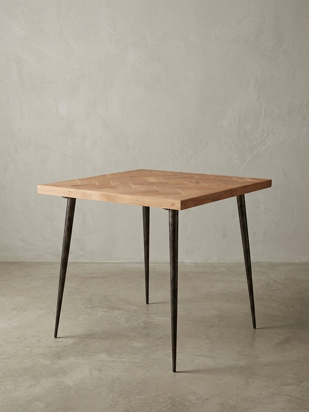 Frontalansicht des quadratischen Esstisches 80x80x76 cm. Die massive Akazienholzplatte mit Fischgrätmuster harmoniert perfekt mit den dunklen, konischen Metallbeinen im Industrial-Design._