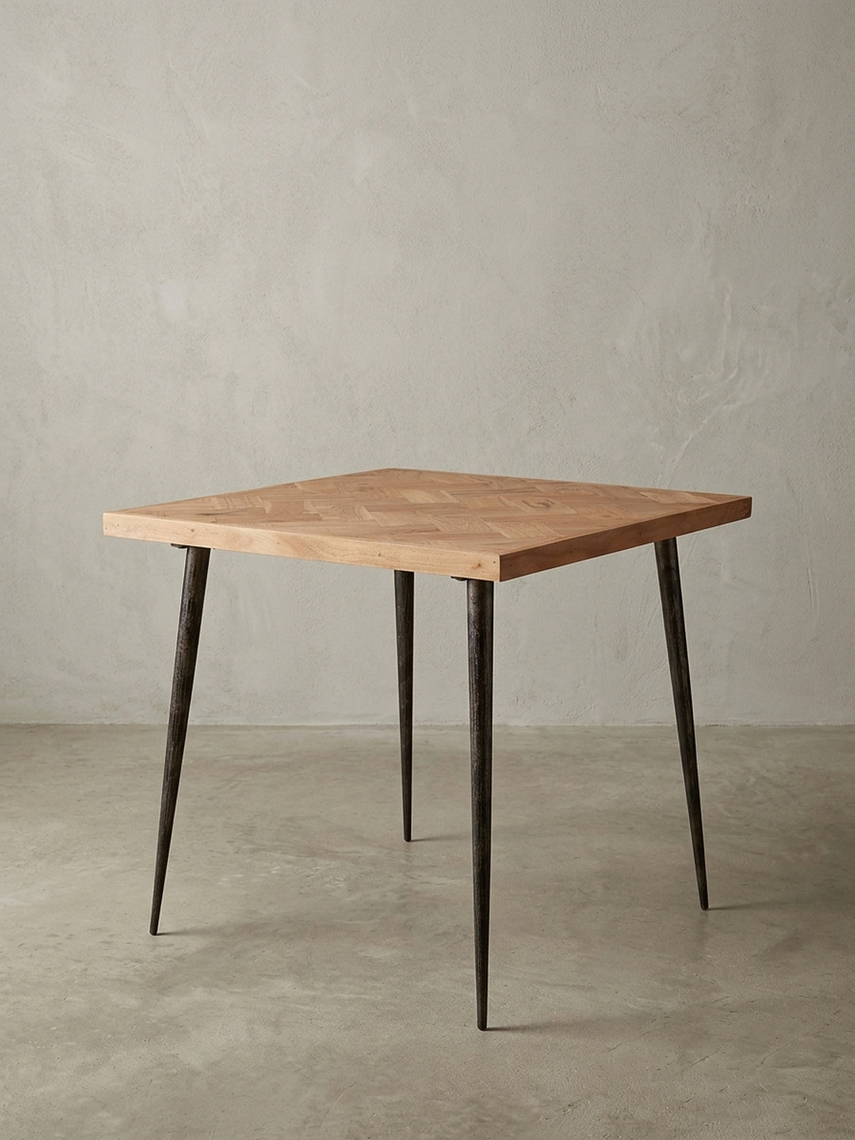 Frontalansicht des quadratischen Esstisches 80x80x76 cm. Die massive Akazienholzplatte mit Fischgrätmuster harmoniert perfekt mit den dunklen, konischen Metallbeinen im Industrial-Design.