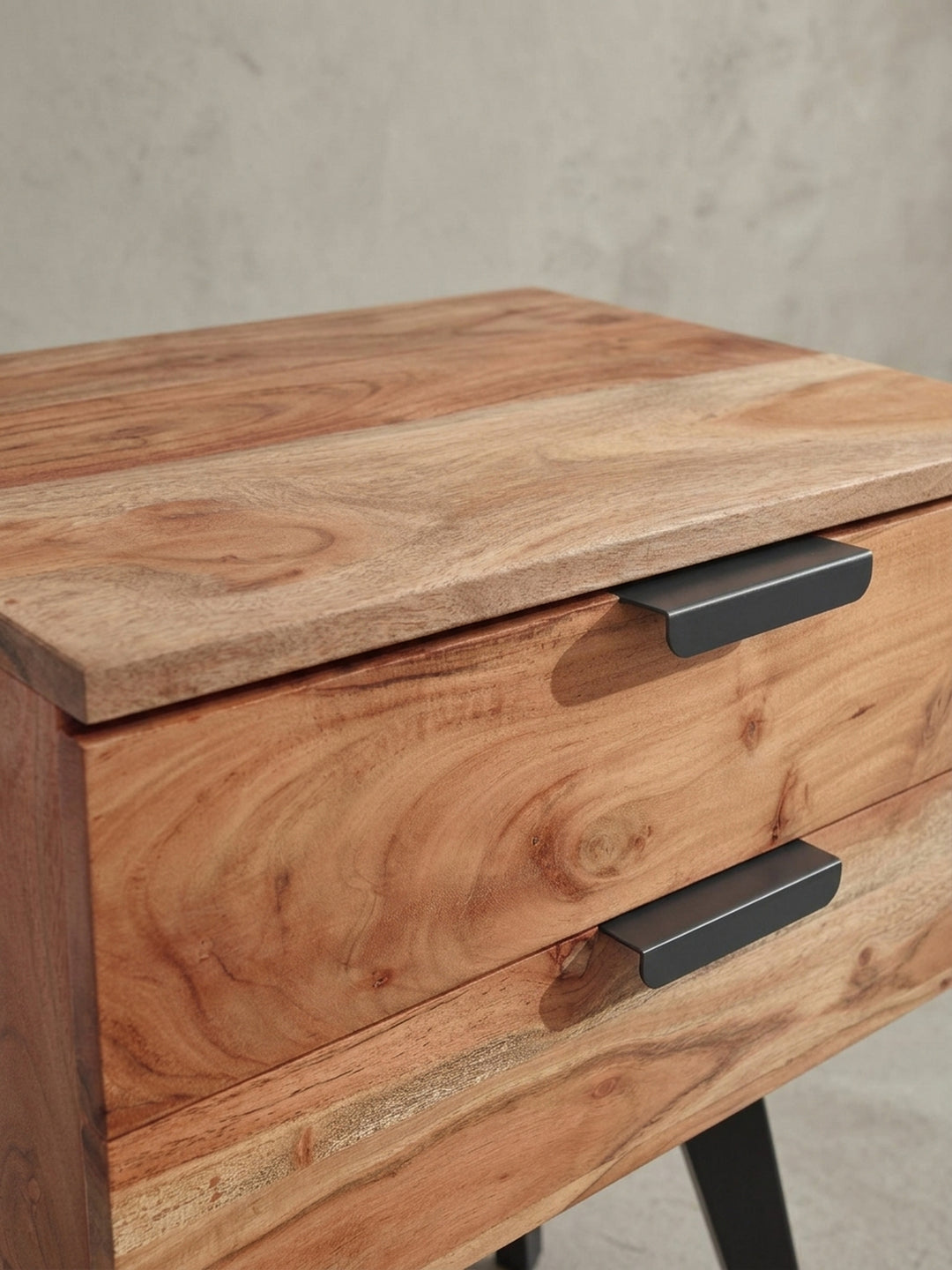 Nahaufnahme eines der minimalistischen, schwarzen Schubladengriffe aus Metall an dem Nachttisch, der einen eleganten Kontrast zum lebhaften Akazienholz bildet._