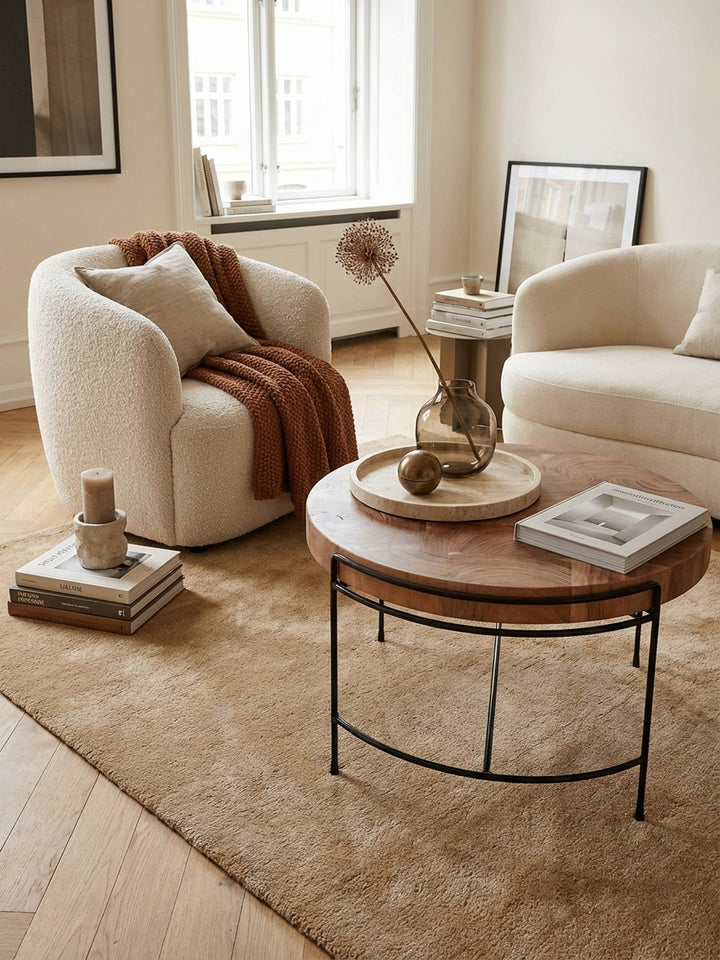Eleganter runder Couchtisch aus massivem Akazienholz in einem hellen, luxuriösen Wohnzimmer, kombiniert mit einem beigen Sofa und einem weichen Wollteppich._