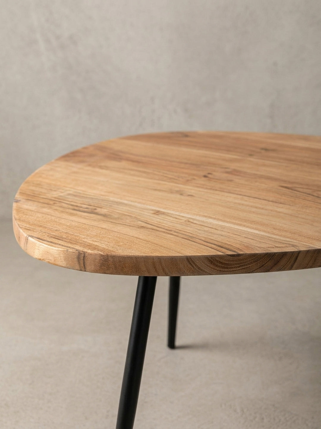 Detailaufnahme des eleganten Designs eines kleinen Couchtischs, fokussiert auf die abgerundete Kante der 2 cm dicken Massivholzplatte und den Ansatz eines schlanken Metallbeins._