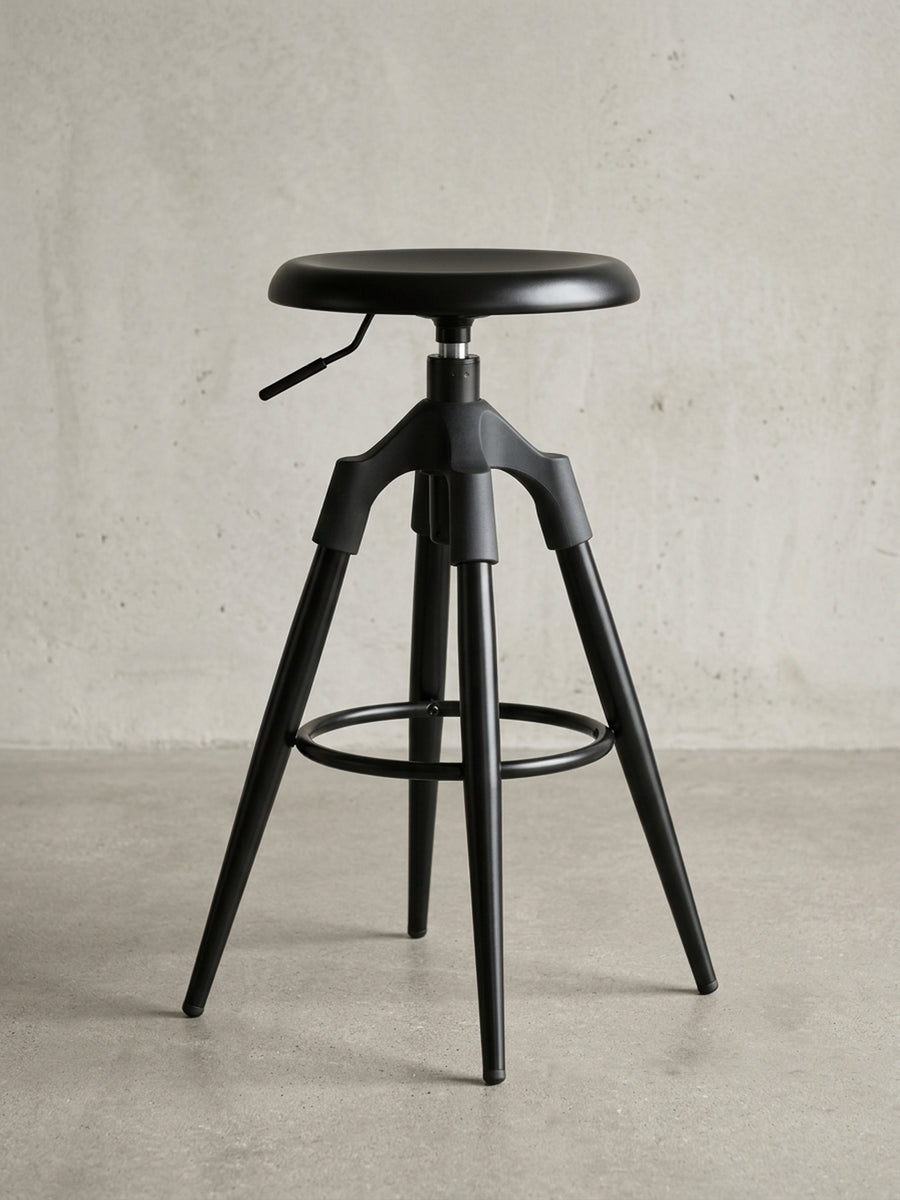 Frontalansicht des industriellen Barhockers aus schwarzem Metall, der sein Dreibein-Gestell und den runden, lehnenlosen Sitz auf weißem Hintergrund präsentiert._
