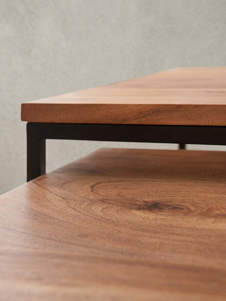 Nahaufnahme der Kante, an der die massive Akazienholzplatte bündig in den mattschwarzen Metallrahmen eingelassen ist, ein Detail des Designs._