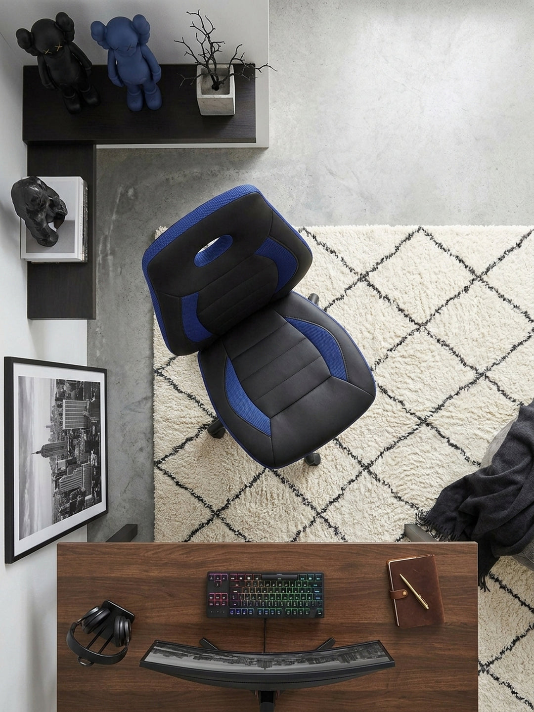 Von schräg oben betrachtet fügt sich der ergonomische Kinderdrehstuhl mit seinem blauen Netzgewebe perfekt in das kühle, architektonische Setup auf dem Sichtbetonboden ein._