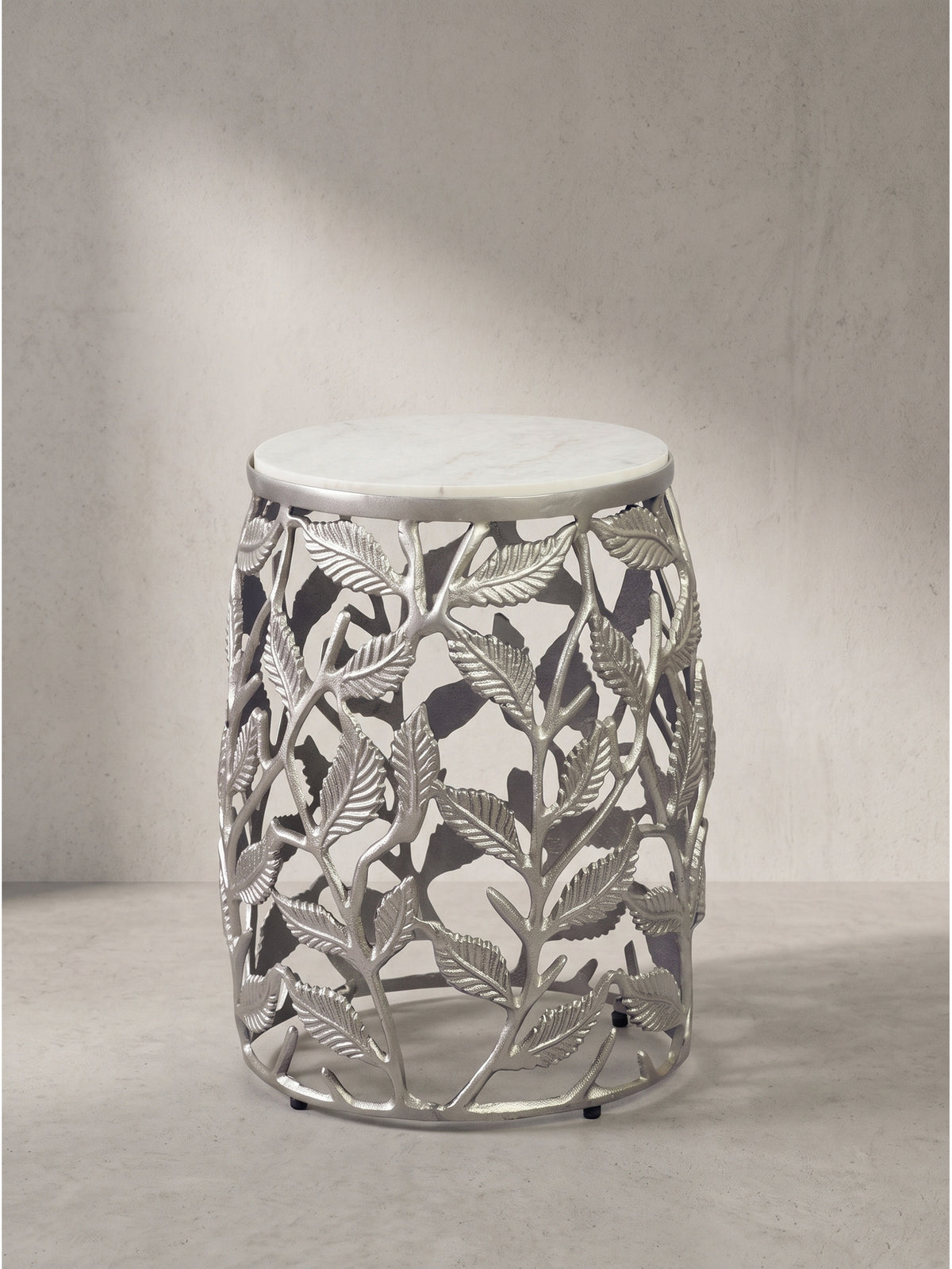 Runder Beistelltisch mit filigranem Blattmotiv-Gestell aus lackiertem Aluminium und weißer Natursteinplatte frontal freigestellt vor weißem Hintergrund.