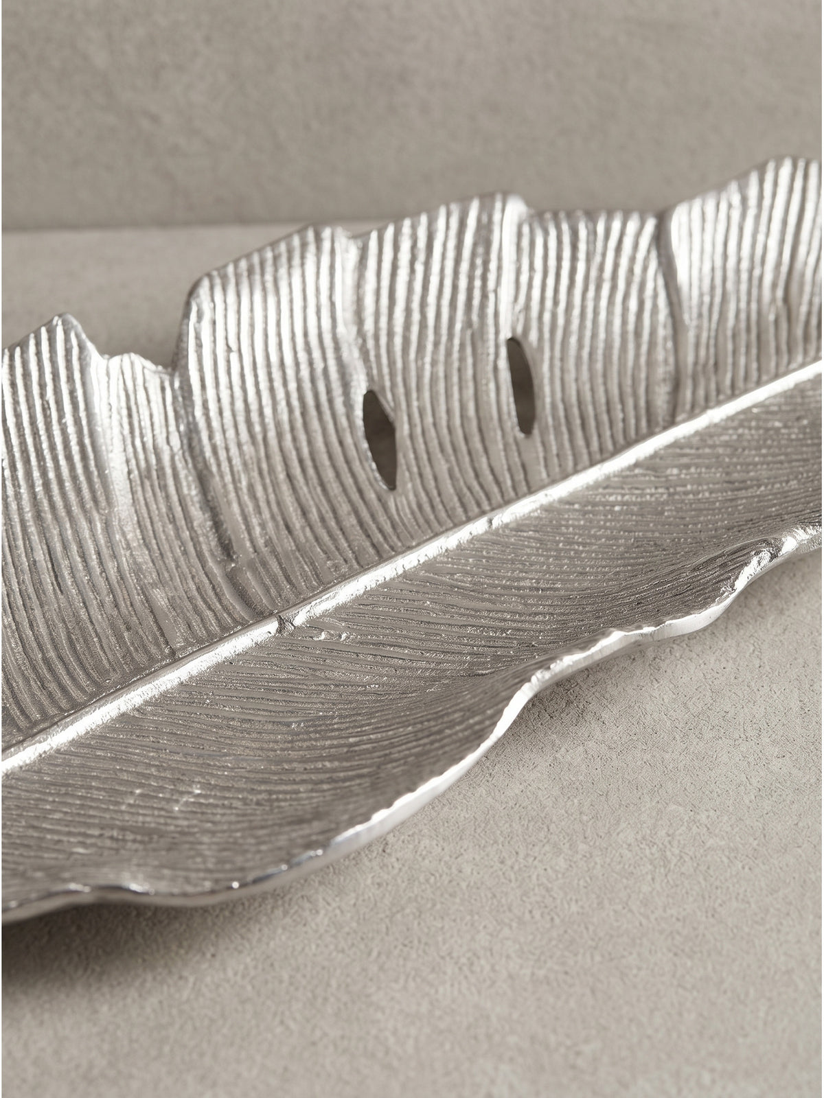 Frontale Schrägansicht der handgefertigten Dekofigur, deren schimmernde Aluminium-Oberfläche das kühle Licht im minimalistischen Raum perfekt reflektiert._