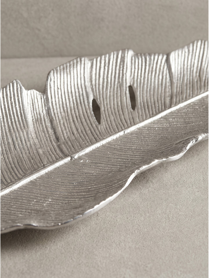 Frontale Schrägansicht der handgefertigten Dekofigur, deren schimmernde Aluminium-Oberfläche das kühle Licht im minimalistischen Raum perfekt reflektiert._
