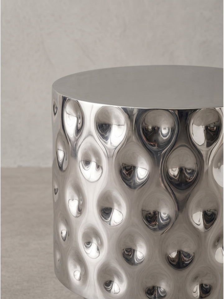 Die Gesamterscheinung des extravaganten Beistelltisches aus glänzendem Aluminium in Silber vereint moderne Formgebung mit traditioneller Metallkunst._