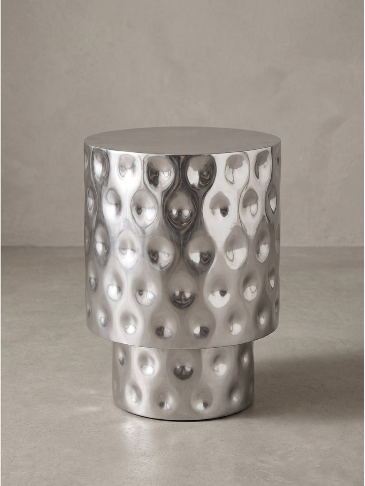 Frontalansicht des runden Beistelltisches aus massivem Aluminium in Silber mit markanter Tropfenprägung und abgestuftem Sockel auf weißem Hintergrund._