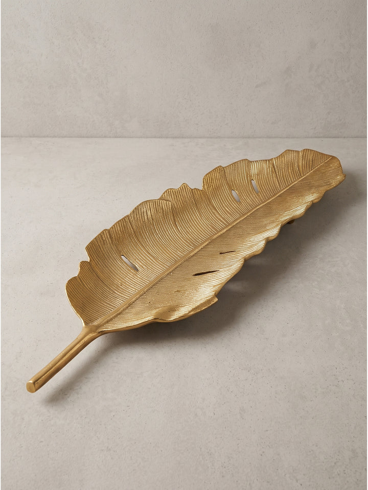 Schräge Seitenansicht der luxuriösen goldenen Dekoschale aus Aluminium, bei der der Stiel als praktischer Griff und das Relief des Tropenblattes gut erkennbar sind._