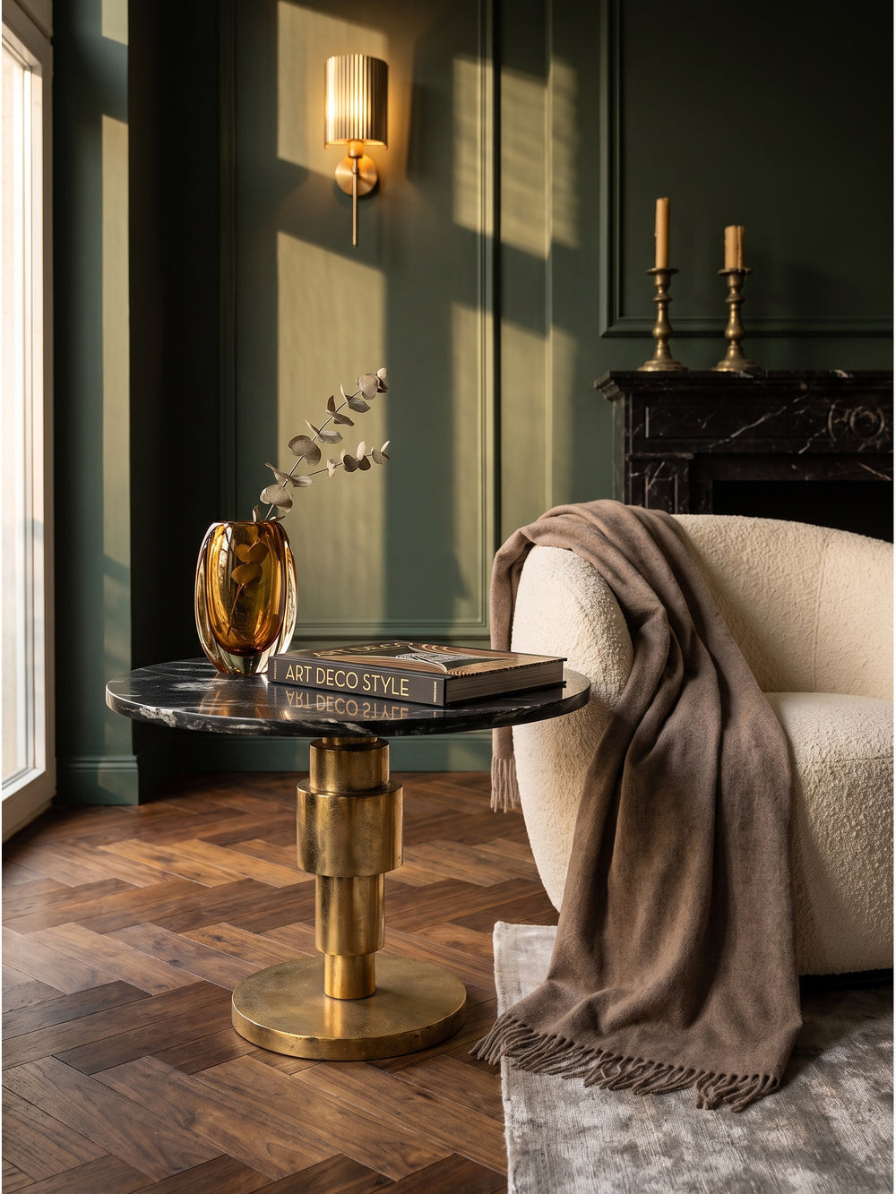 Ein schwerer Bildband und eine weiße Espressotasse auf dem eleganten Beistelltisch aus schwarzem Marmor und Gold im gemütlichen Wohnzimmer._