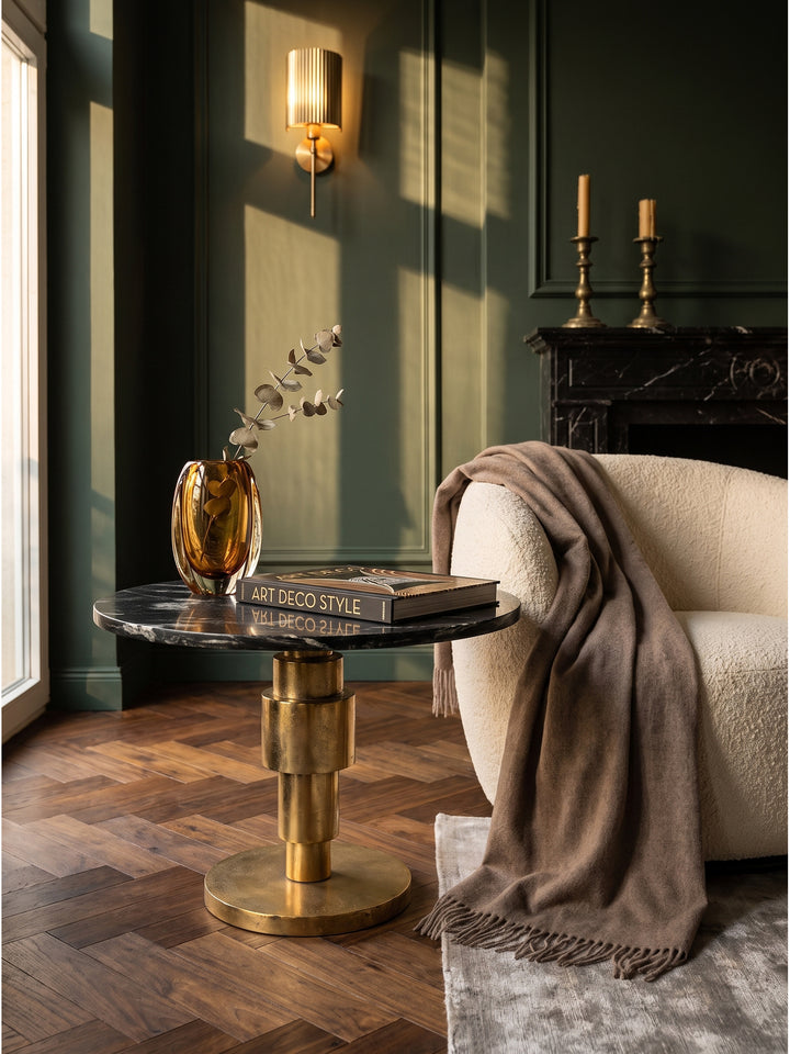 Ein schwerer Bildband und eine weiße Espressotasse auf dem eleganten Beistelltisch aus schwarzem Marmor und Gold im gemütlichen Wohnzimmer._