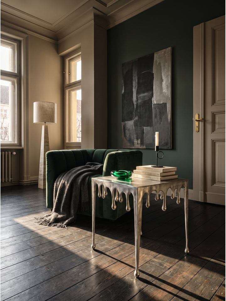Skulpturaler Beistelltisch aus lackiertem Aluminium in Silber 45,5x45,5x51 cm im Art-Deco Wohnzimmer neben einem dunkelgrünen Samtsessel_