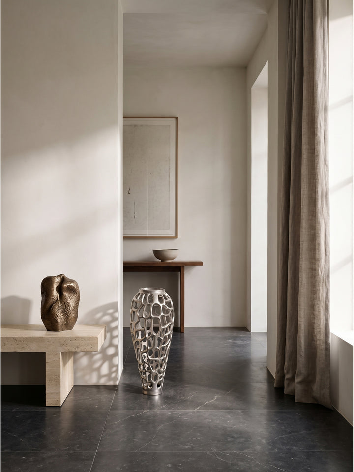 Elegante 60cm hohe Aluminium-Blumenvase kombiniert mit einem puristischen Lowboard und minimalistischer Schwarz-Weiß-Fotografie an einer warmweißen Wand_