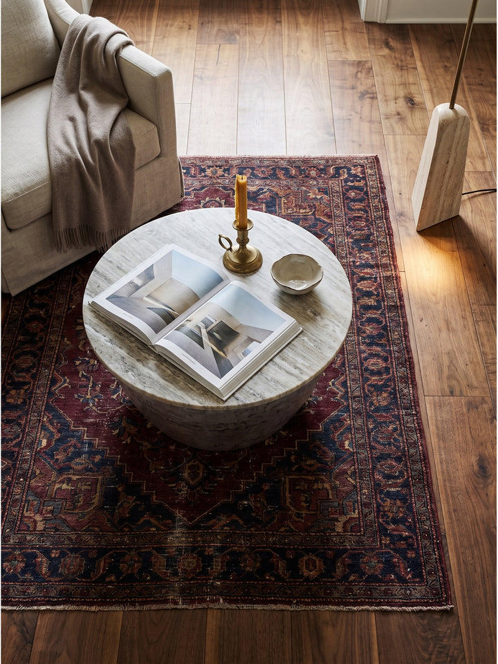 Draufsicht auf einen runden Wohnzimmertisch aus Metall und Marmor im modernen Design arrangiert mit dunkelgrauem Samtsofa auf einem Vintage Perserteppich_