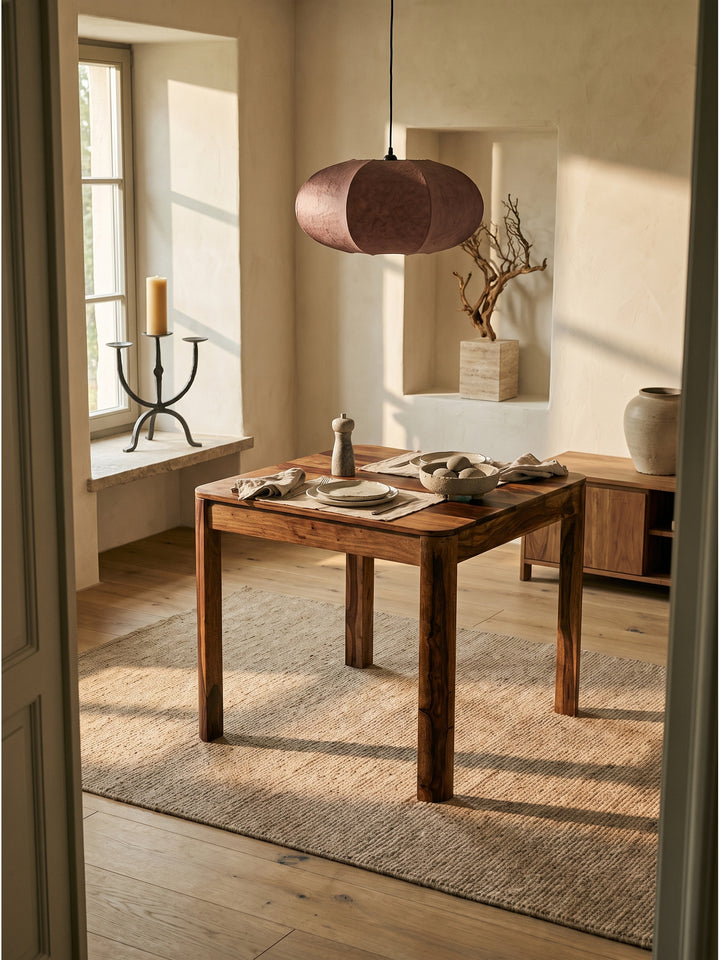 Quadratischer Esstisch aus Sheesham Massivholz im Organic Modern Stil auf hellem Holzboden unter einer Papier-Pendelleuchte._