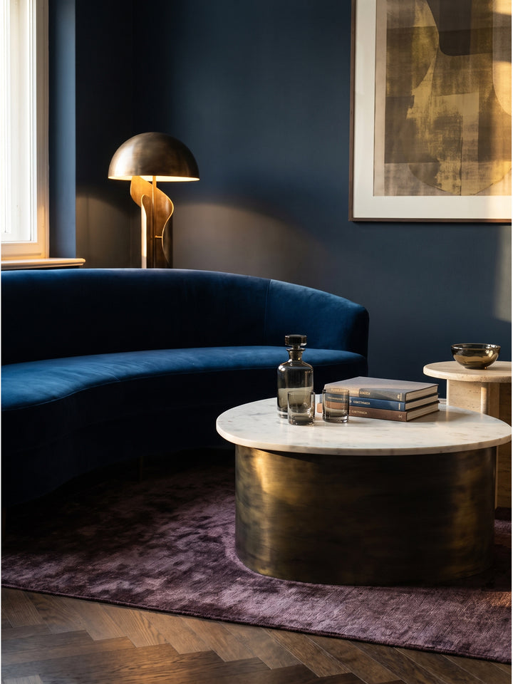 Design Couchtisch organische Form Aluminium und Marmor kombiniert mit Samt-Sofa im dunklen Interieur auf Walnuss-Parkett_