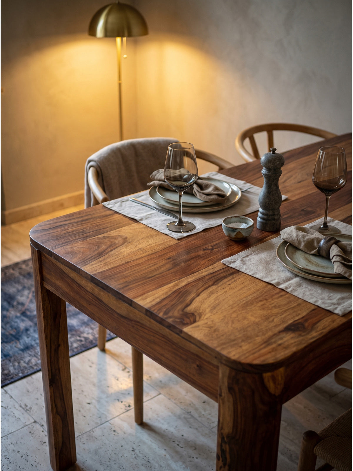 Gemütliches Ambiente am Holztisch mit handgefertigter Keramikvase und getrockneten Olivenzweigen vor einer warmweißen Wand_