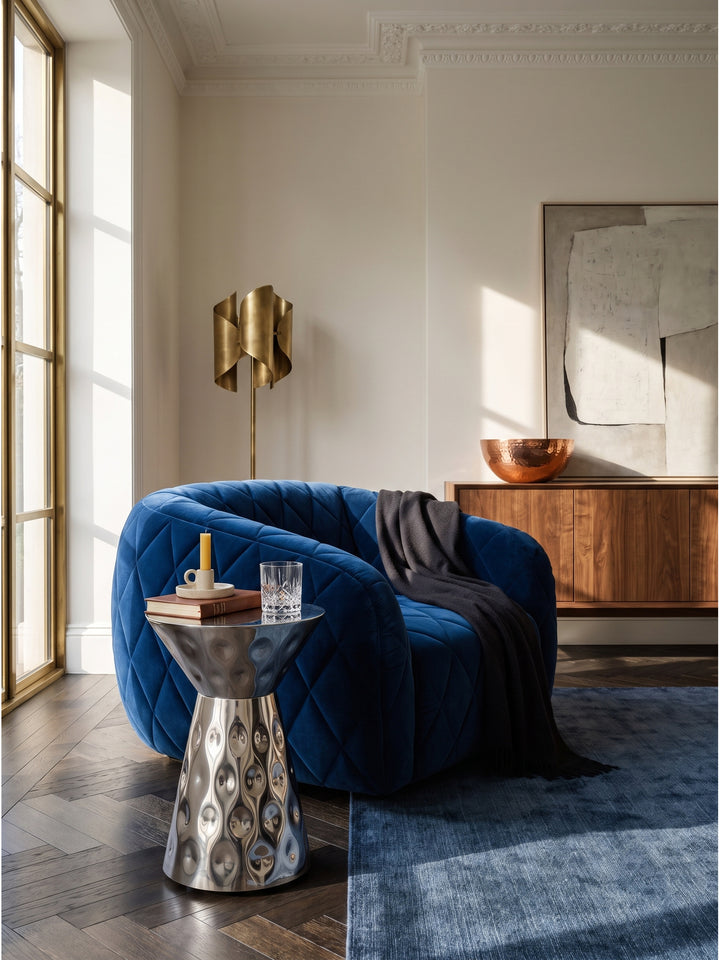 Silberner Designer Anstelltisch aus Aluminium kombiniert mit einem dunkelblauen Samtsessel in einem elegant eingerichteten Wohnzimmer._