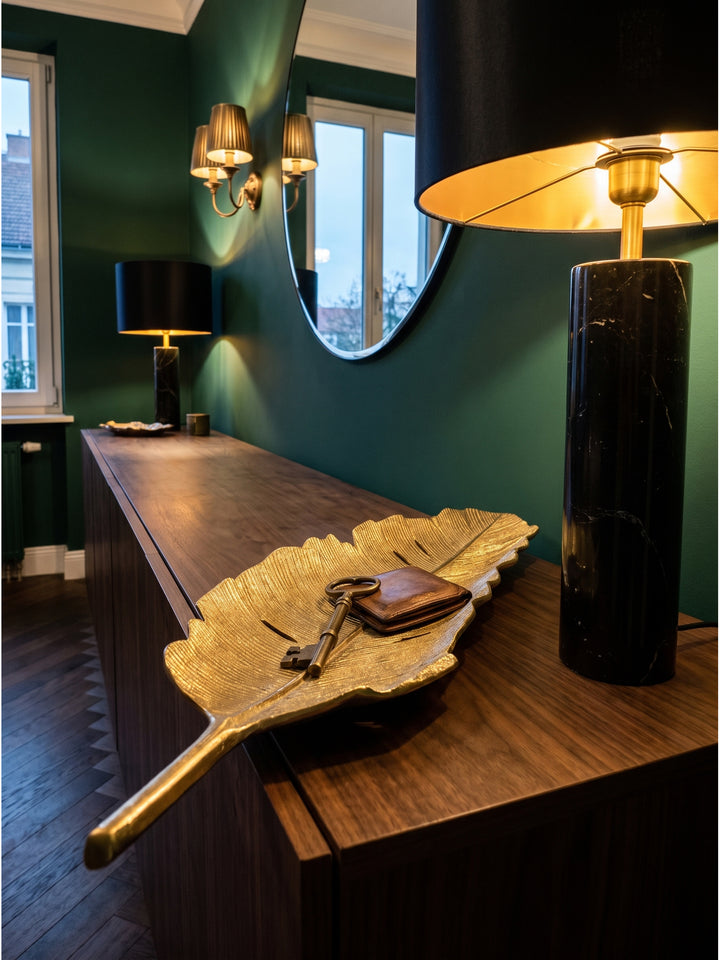 Die geschwungene goldene Aluminium-Schale im Blattdesign dient als großzügige Ablage für Alltagsgegenstände und Schmuck neben einer schweren Marmorlampe im Schlafzimmer._