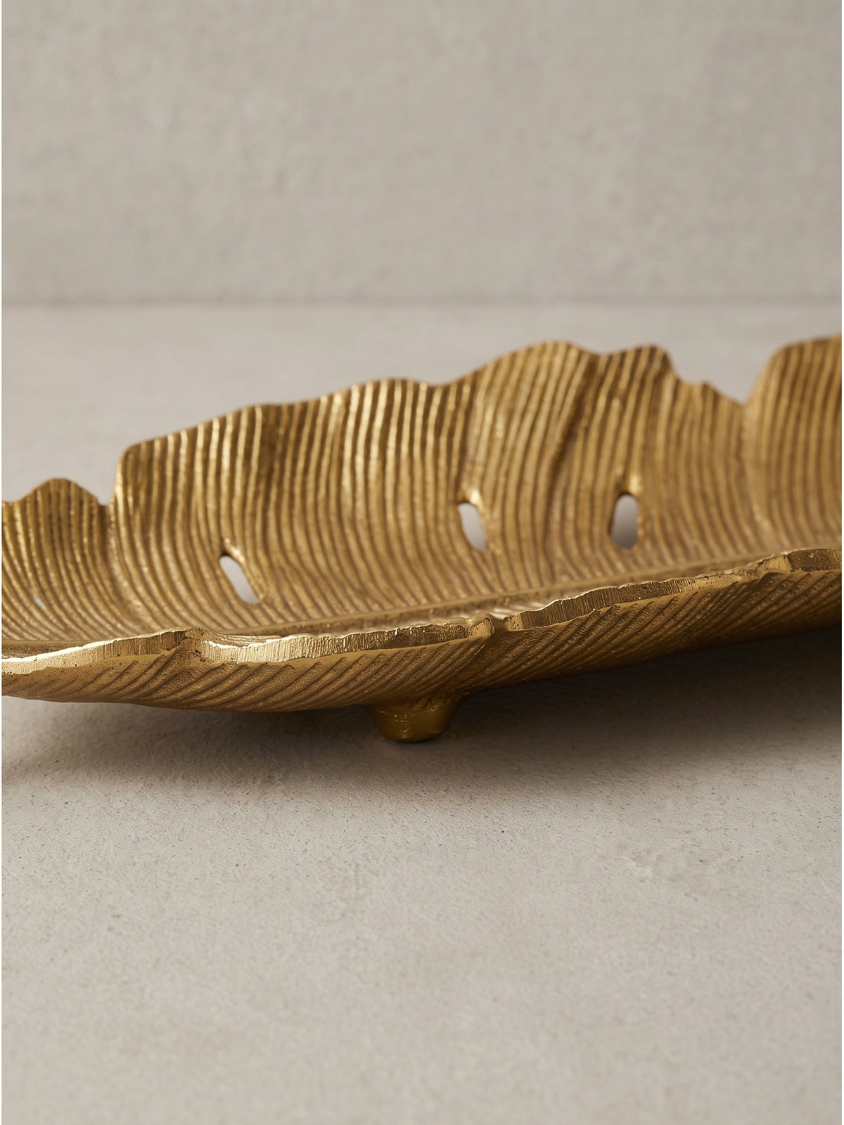 Detailreiche Aufnahme der goldenen Oberfläche aus lackiertem Aluminium, die durch feine Unebenheiten den Unikat-Charakter der großen dekorativen Blattschale unterstreicht._
