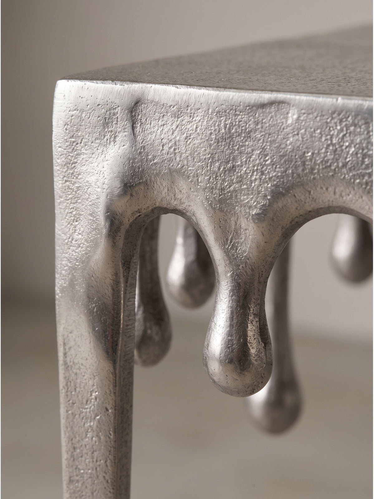 Nahaufnahme der strukturierten Aluminiumoberfläche des silbernen Beistelltisches mit organischen Tropfendetails_