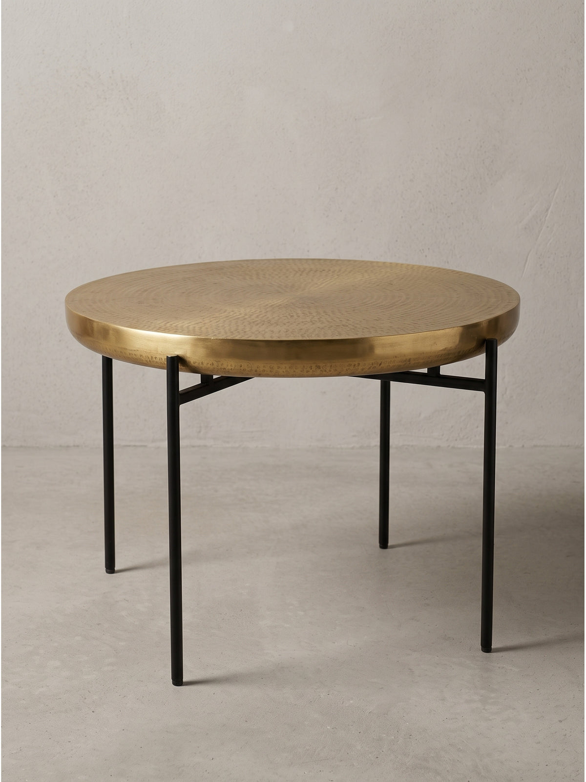 Freigestellter Couchtisch mit runder Aluminiumplatte in Gold und vier schlanken schwarzen Eisenbeinen in Frontalansicht_