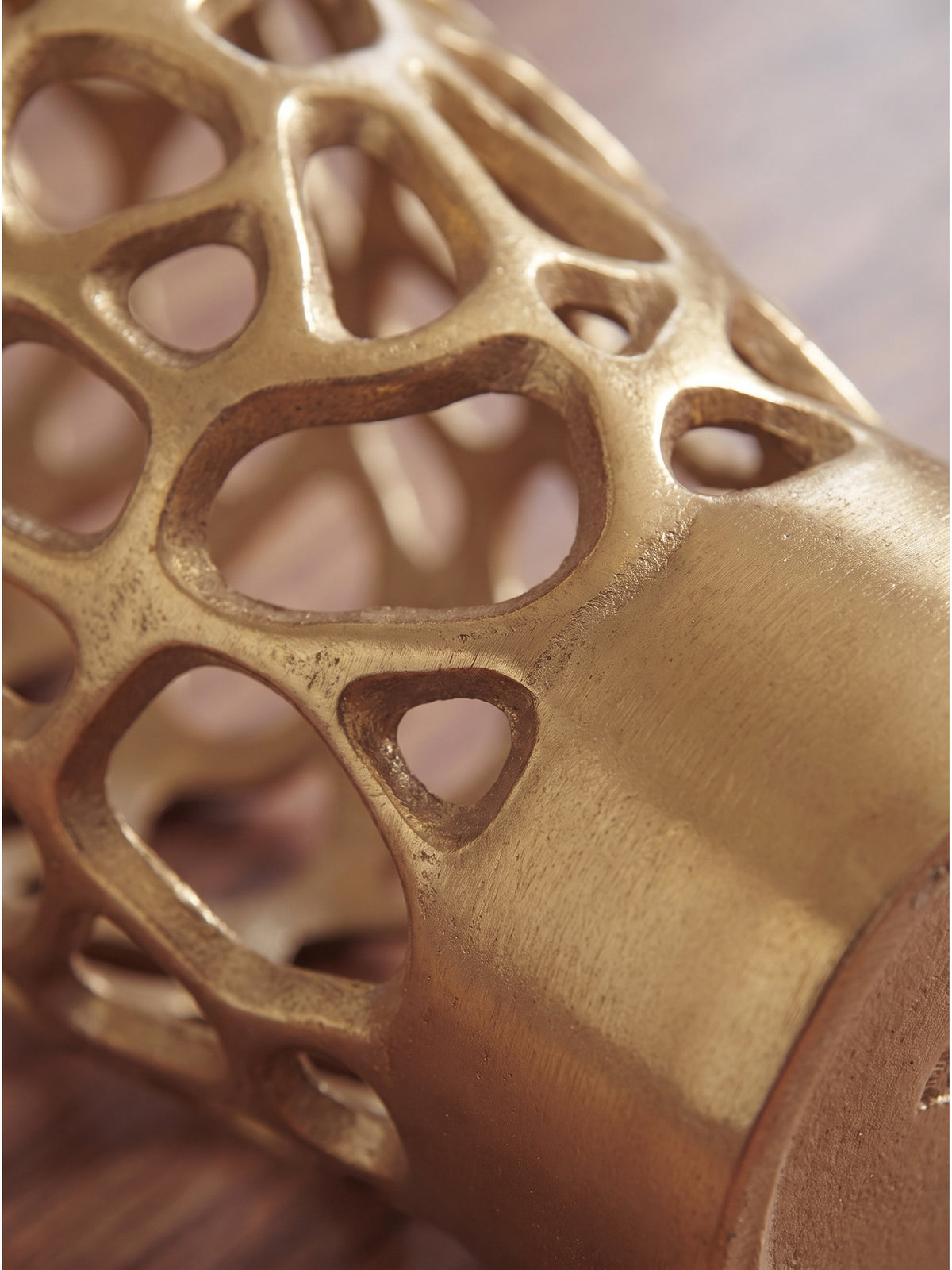 Nahaufnahme der filigranen Gitterstruktur der handgefertigten Aluminiumvase in Gold mit feinem metallischen Glanz und subtilem Lichtspiel_