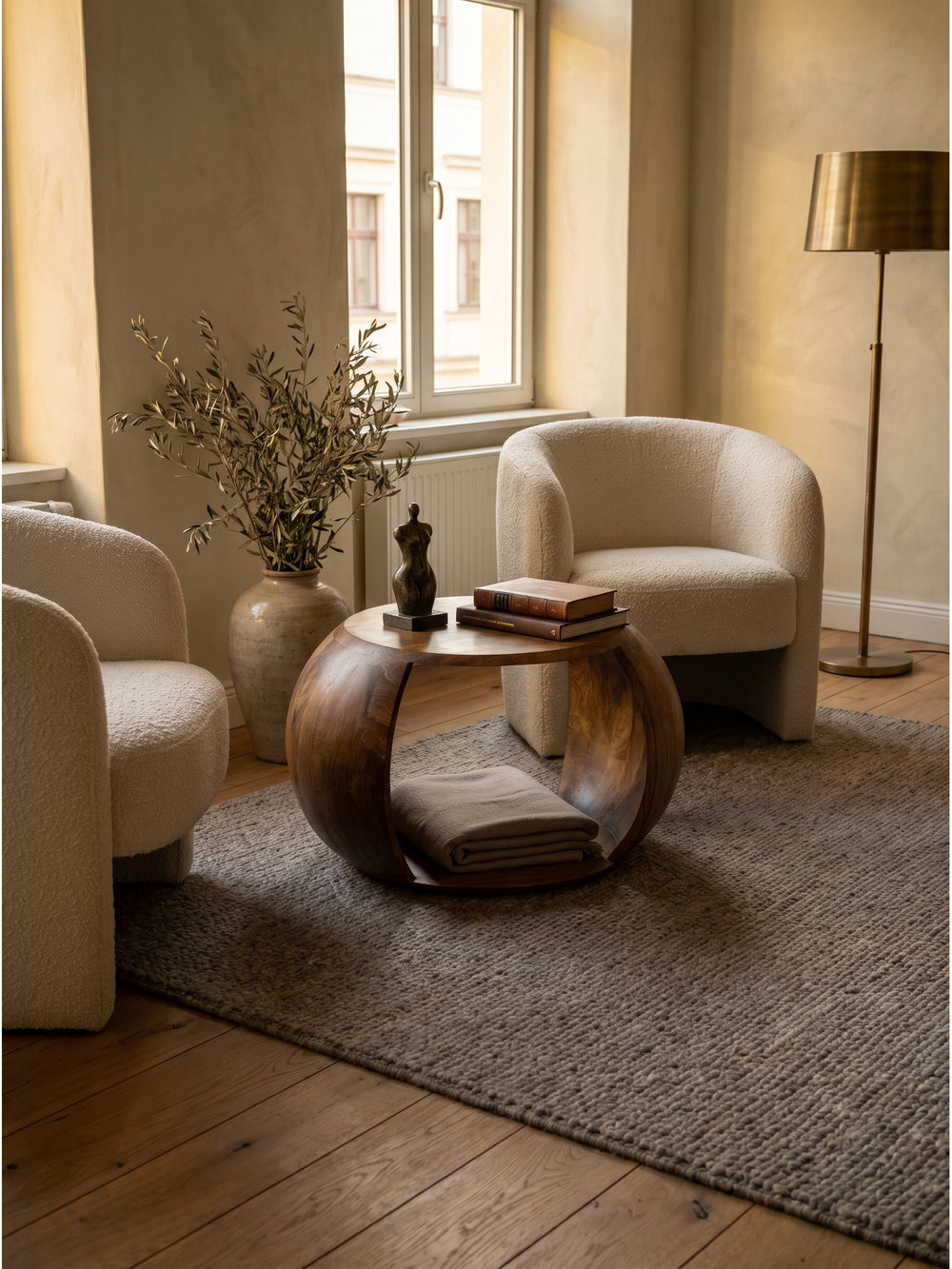 Skulpturaler runder Couchtisch aus Mango Massivholz im organisch-modernen Wohnzimmer auf hellem Eichenparkett zwischen zwei cremefarbenen Bouclé-Sesseln_