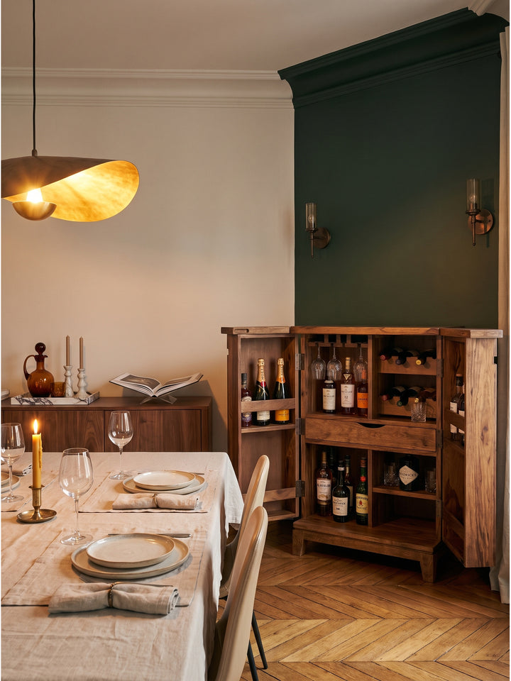 Ein bernsteinfarbener Whiskey in einem Kristallglas steht auf der aufgeklappten Hausbar aus massivem Sheeshamholz neben einer schweren Messinglampe._