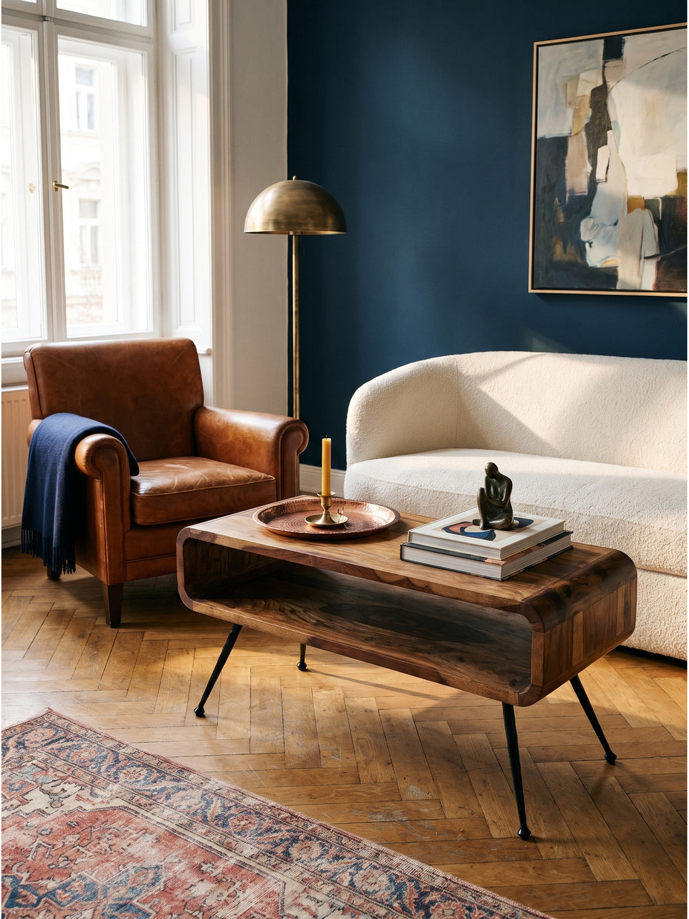 Ein Ledersessel im Mid-Century Design ergänzt den warmen Sheesham Massivholz Couchtisch im Vintage-Modern Stil hervorragend auf dem Fischgrätparkett._