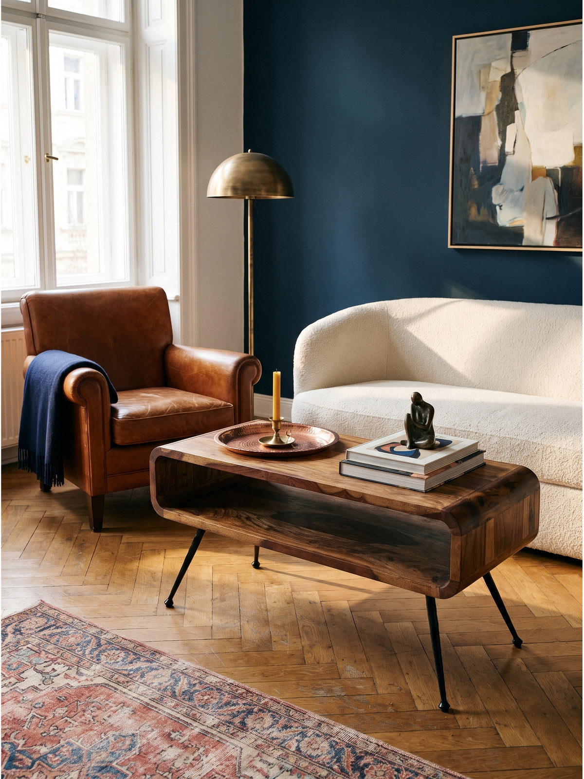 Ein Ledersessel im Mid-Century Design ergänzt den warmen Sheesham Massivholz Couchtisch im Vintage-Modern Stil hervorragend auf dem Fischgrätparkett._