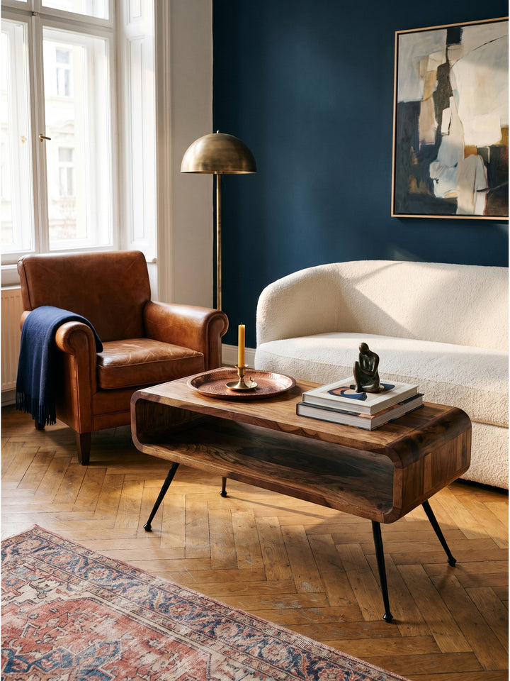 Ein Ledersessel im Mid-Century Design ergänzt den warmen Sheesham Massivholz Couchtisch im Vintage-Modern Stil hervorragend auf dem Fischgrätparkett._