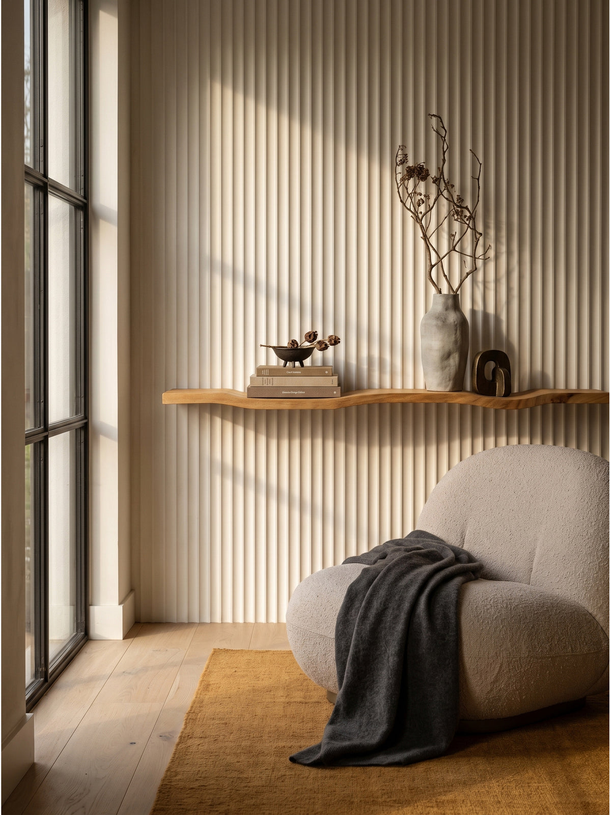 Schwebendes Wandregal aus Akazie Massivholz 100cm an einer strukturierten Putzwand über einem sandfarbenen Bouclé-Sessel im ruhigen Wohnzimmer_