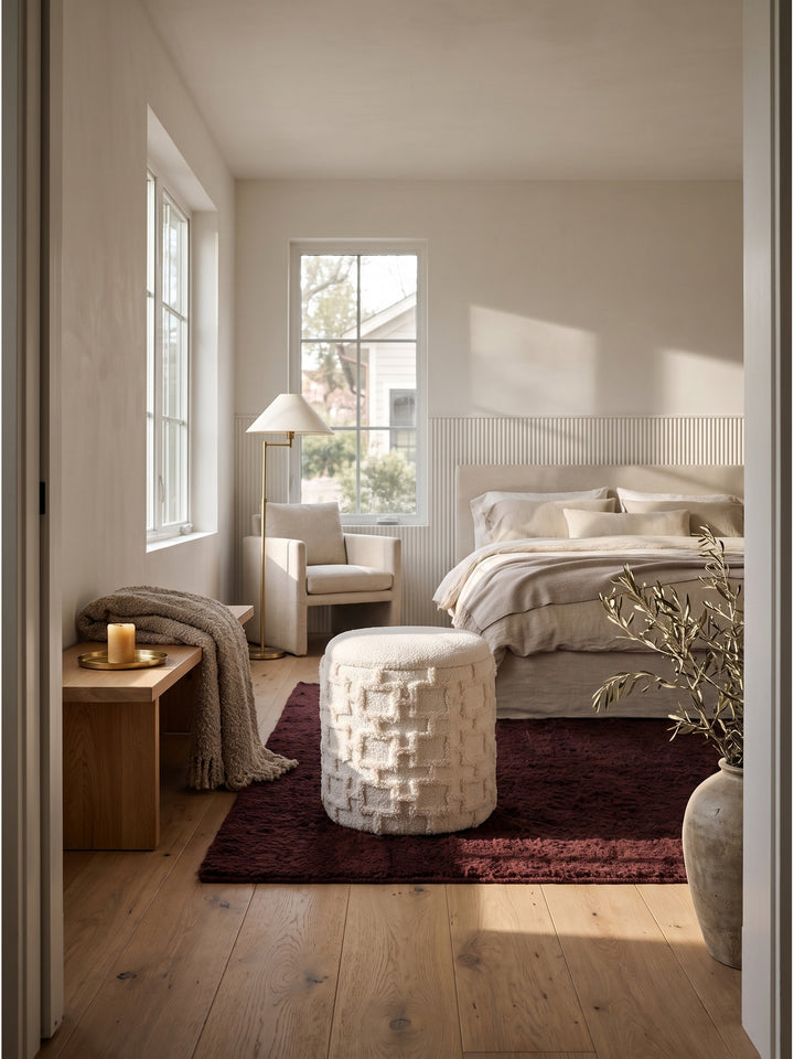 Runder Polsterhocker in Creme mit Strukturstoff im organisch-modernen Schlafzimmer auf breiten Eichendielen._