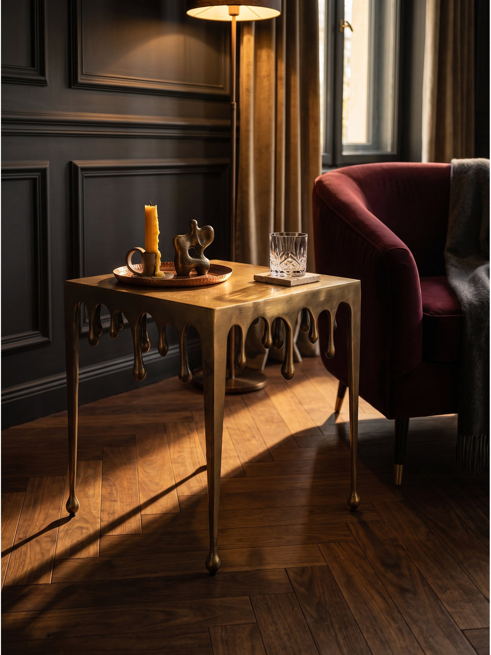 Goldener Couchtisch mit fließender Optik dekoriert mit einem Kristallglas und Büchern im eleganten Lounge-Bereich_